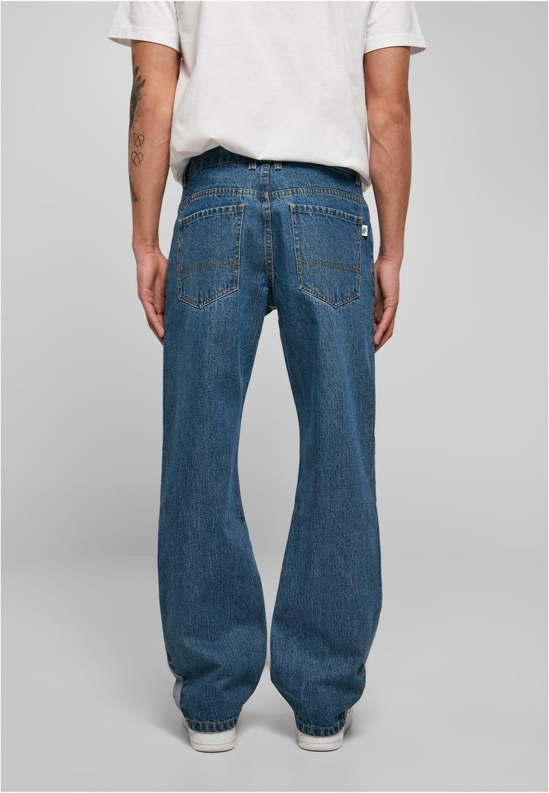 Niebieskie dżinsy z denimu o luźnym kroju, z dwoma tylnymi kieszeniami i subtelnymi przeszyciami, zestawione z białymi trampkami.