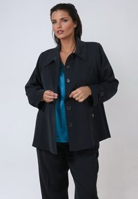 Black outer coat with a structured design, featuring a large collar, front buttons, and oversized sleeves. Worn over a teal top.