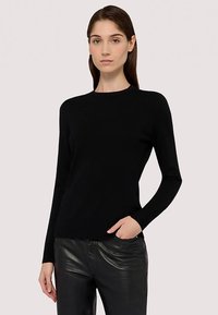 Svart långärmad tröja av mjukt tyg med rund halsringning, figurnära siluett och minimalistisk design. Bärs med svarta läderbyxor.