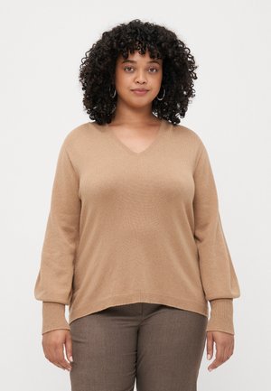 Beige V-hals genser med løs passform og ribbestrikkede mansjetter. Mykt stoff med glatt tekstur, vist sammen med brune bukser.