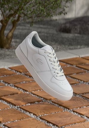 White leather sneaker with a smooth texture, round toe, and flat laces. Features a subtle logo on the side and a cushioned interior.