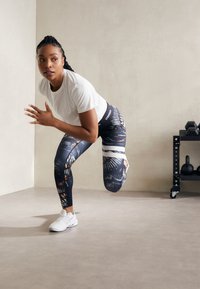 Sorte og blå leggings med mønster prydes af farverige accenter og en hvid stribe, og sættes sammen med en simpel hvid t-shirt og hvide træningssko.