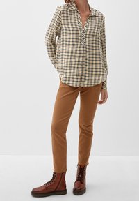 Camicia di cotone a quadri in giallo, blu navy e bianco; maniche lunghe con colletto e chiusura a bottoni. Pantaloni in velluto a coste slim-fit marroni e stivali con lacci.