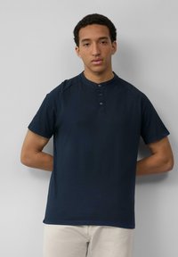 Navyblauw polo shirt met korte mouwen, een hoge kraag en een drie knopen sluiting. Zachte stof met een gladde textuur, ontspannen pasvorm.