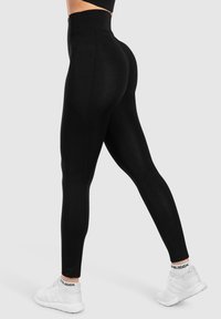 Zwarte hooggewaisted legging gemaakt van rekbare stof met een gladde textuur en een aansluitend ontwerp, gecombineerd met witte sport schoenen.