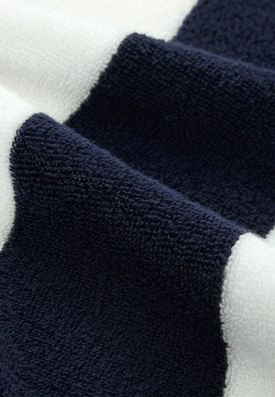 Gros plan sur un tissu en éponge texturé bleu marine et blanc avec des bords pliés et des boucles visibles.