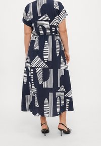 Vestido maxi azul marino con patrones abstractos en blanco, mangas cortas, cintura elasticada y una falda fluida. Sandalias de tacón alto negras con tirantes.