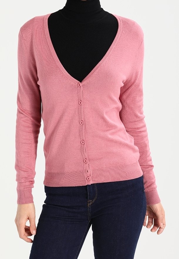 Femme portant un cardigan rose ajusté boutonné sur un col roulé noir, associé à un jean bleu foncé.