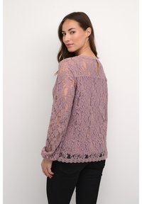 Spitzenoberteil in staubigem Rosé mit langen Ärmeln, einem Schlüsselrücken und gewelltem Saum. Verfügt über florale Muster und eine weiche, strukturierte Oberfläche.