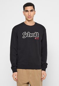 Felpa nera con colletto tondo, caratterizzata da un grande logo bianco "Schott" e "N.Y.C" in rosso. Realizzata in un tessuto morbido e testurizzato.