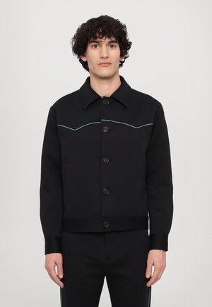 Black jacket with a collar, front pockets, and buttons. Features contrasting green stitching in a curved design along the chest.