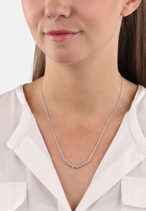 Collana in argento con un design curvo che presenta piccole perle rotonde, indossata su un collo nudo sopra una blusa bianca.