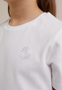 Vit bomull t-shirt med en diskret broderad tusensköna-detalj på bröstet. Klassisk rund halsringning och korta ärmar. Slät textur.