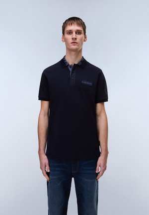 Polo bleu marine à la texture douce, avec une patte de boutonnage à trois boutons, petit logo sur la poitrine et détail contrastant sur le col. Porté avec un jean bleu.