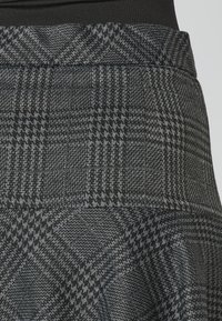 Falda de cuadros con un patrón tejido en negro y gris, una cintura estructurada y un tejido texturizado, que enfatiza formas geométricas.