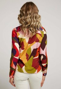 Chemise à manches longues avec un imprimé abstrait aux couleurs vives, comprenant du rouge, du violet et du jaune. Tissu texturé avec des accents de boutons.