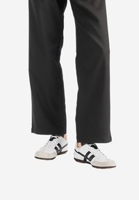 Witte en zwarte sportschoenen met suède accenten, gedragen met zwarte wijde broeken. De schoenen hebben veters en een profielzool.