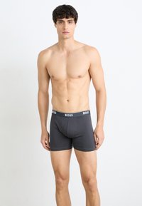 Graue Boxer-Shorts aus glattem Baumwollstoff, mit einem schwarzen Bund und dem "BOSS"-Logo. Enganliegendes Design mit einer Länge bis zur Mitte des Oberschenkels.