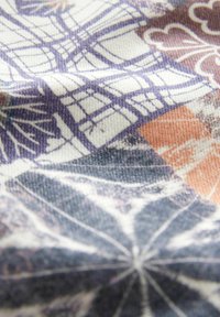 Textilní látka se detailním vzorem v purpurové, oranžové a černé barvě. Design zahrnuje geometrické tvary a organické motivy.