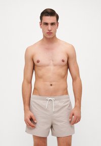 Shorts de bain beiges clairs en tissu texturé, avec une taille élastique et un cordon blanc. Le design est simple, sans motifs ni accents.