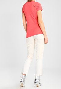 Koralli lyhythihainen kapea T-paita esillä takaa, yhdistettynä vaaleisiin farkkuihin ja metallinvärisiin nilkkap bootseihin. Sileä kangas.