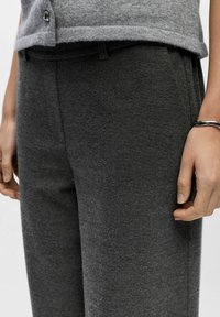 Grå uldblandede bukser med en glat tekstur, der har forlommer og diskrete syninger, suppleret af en matchende grå strikbluse.