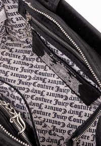 Interno di una borsa in velluto nero che presenta diverse tasche con cerniera, una fodera in satin con logo in bianco e nero e dettagli in hardware argentato.