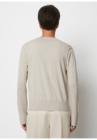 Beżowy sweter z długimi rękawami, okrągłym dekoltem i ściągaczem na dole. Gładka faktura z subtelnymi różnicami kolorystycznymi. Prosty design.