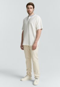 Biała bawełniana koszula z krótkim rękawem z niebieskim akcentem kołnierza i listwą z trzema guzikami, w połączeniu z jasnobeżowymi spodniami i białymi trampkami.