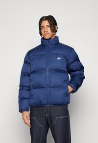 Ναυτικό μπουφάν με ψηλό γιακά, κλείσιμο με φερμουάρ και ραμμένα πάνελ. Διαθέτει το μικρό άσπρο λογότυπο της Nike στο αριστερό στήθος.