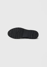 Semelle de chaussure en caoutchouc noir avec des rainures profondes et des motifs texturés pour une meilleure adhérence. Design plat avec des bords arrondis, adapté pour une utilisation décontractée.