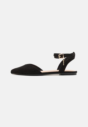 Chaussure plate noire pour femmes avec bout pointu, bride cheville avec boucle dorée et petit pendentif suspendu, en suède, vue de côté.