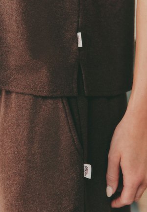 Brown fabric top with layered design and small white label detail, featuring a textured finish and side slits.