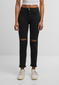 Černé džíny s vysokým pasem, s roztrhnutými koleny a surovými lemy, vyrobené z denimové látky. Doplněné o bílé tenisky a krátký top.