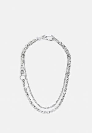 Collier à double chaîne en argent avec des maillons variés et un fermoir mousqueton sur un fond blanc uni.