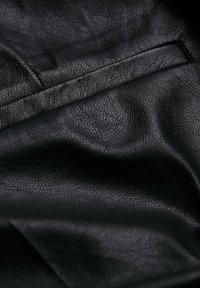 Tissu en cuir synthétique noir avec une surface texturée, présentant de légères plis et un éclat lisse, indiquant flexibilité et durabilité.