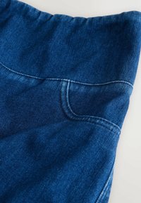 Țesătură din denim de culoare albastră închisă, cu o textură netedă. Prezintă un brâu curbat cu un buzunar, evidențiat de cusături contrastante pe marginile acestuia.