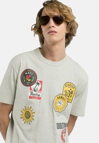 T-shirt in cotone grigio chiaro con diverse toppe colorate – sole, palme e nomi di località. Collo a giro e maniche corte.