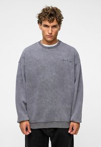 Grijze oversized sweatshirt met een ronde halslijn en verlaagde schouders, voorzien van een subtiele logodetail op de borst, gemaakt van zachte stof.