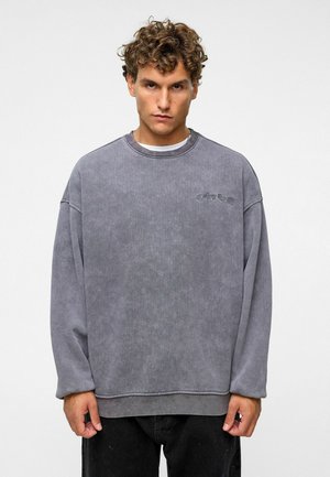 Grijze oversized sweatshirt met een ronde halslijn en verlaagde schouders, voorzien van een subtiele logodetail op de borst, gemaakt van zachte stof.