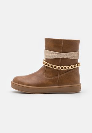 Brun støvle til midt på læggen med flad sål, dekoreret med en beige indpakning og en guldkæde omkring anklen.