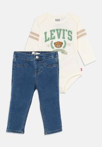 Levi's babykläder som består av en krämfärgad långärmad bodysuit med grön logotyp och beige ränder, i kombination med blå denimbyxor.