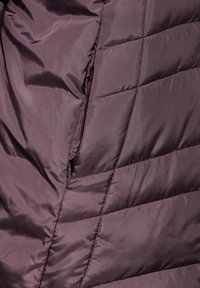 Mörklila puffjacka i tyg med en slät, glänsande yta och diagonalt quiltat mönster, med sömmar som är sydda och lätt isolering.
