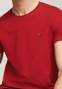 Rød bomulds t-shirt med rund halsudskæring og korte ærmer. Har et lille broderet logo i blå og hvid på venstre bryst.