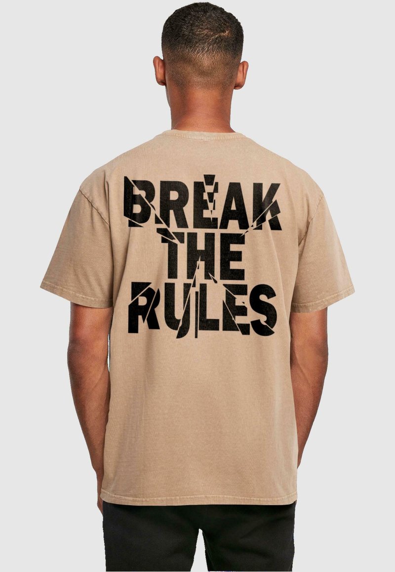 Beige t-shirt med korte ærmer, der har fed sort tekst på ryggen, som siger "BRYDE REGULERNE" med en slidt, revnet effekt.