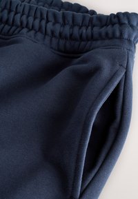 Tengerészkék kötött melegítőnadrág elasztikus derékpánttal, oldalzsebekkel és texturált anyaggal, sima felülettel és kényelmes, bő szabással.