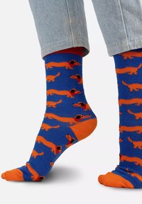 Niebieskie skarpetki z wzorem w pomarańczowego jamnika, z czarnymi akcentami, prezentujące kontrastowy pomarańczowy palec i mankiet. Wykonane z mieszanki bawełny.