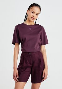 Maroon short-sleeve t-shirt with a round neckline and embroidered logo. Paired with high-waisted maroon shorts featuring a button closure.