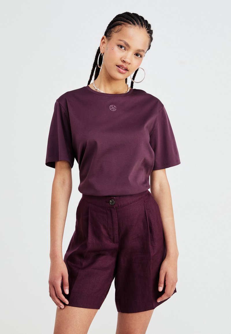 Maroon short-sleeve t-shirt with a round neckline and embroidered logo. Paired with high-waisted maroon shorts featuring a button closure.
