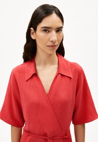 Rotes Leinen-Wickelkleid mit Kragen, kurzen Ärmeln und einem Bindeband in der Taille. Der Stoff hat eine strukturierte Oberfläche und einen weichen Fall.